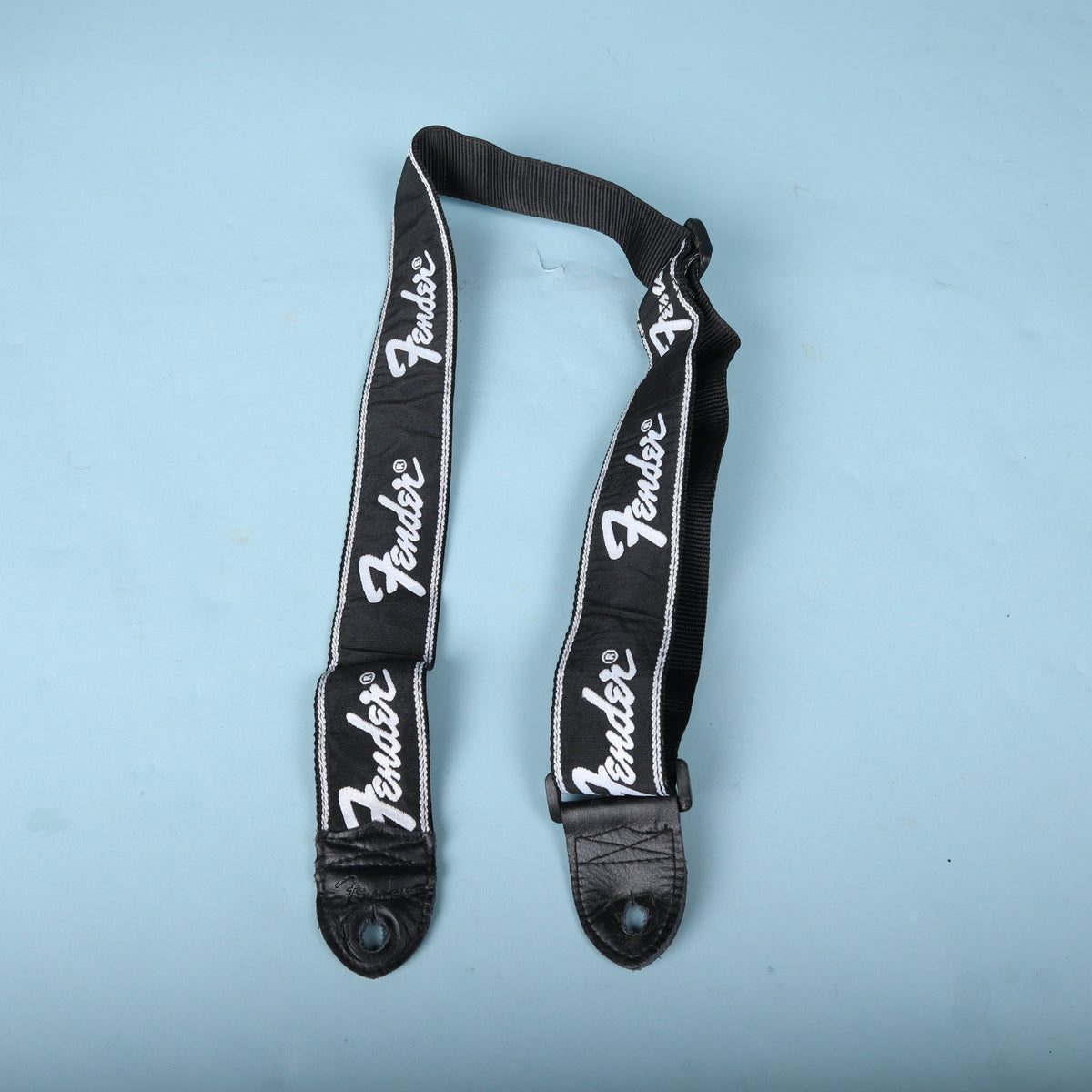 Fender running logo guitar strap laid out showing repeating white logos and leather ends