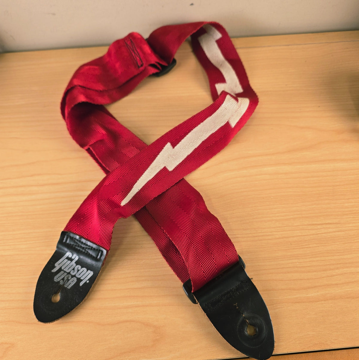 Gibson Lightning Bolt guitar strap in red laid out on a wooden surface