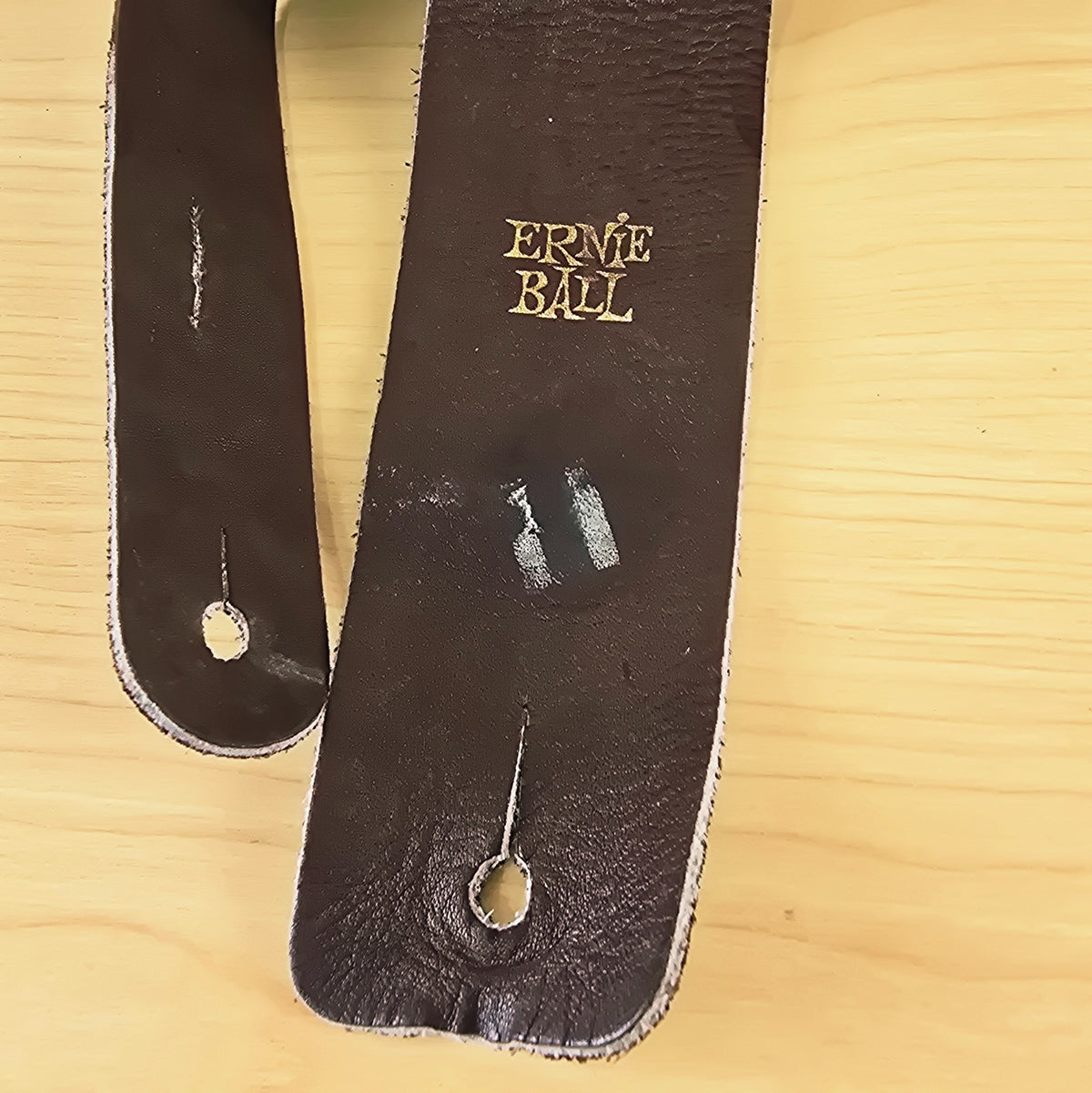 Close-up of the gold Ernie Ball logo stamp and front endpin hole on brown leather