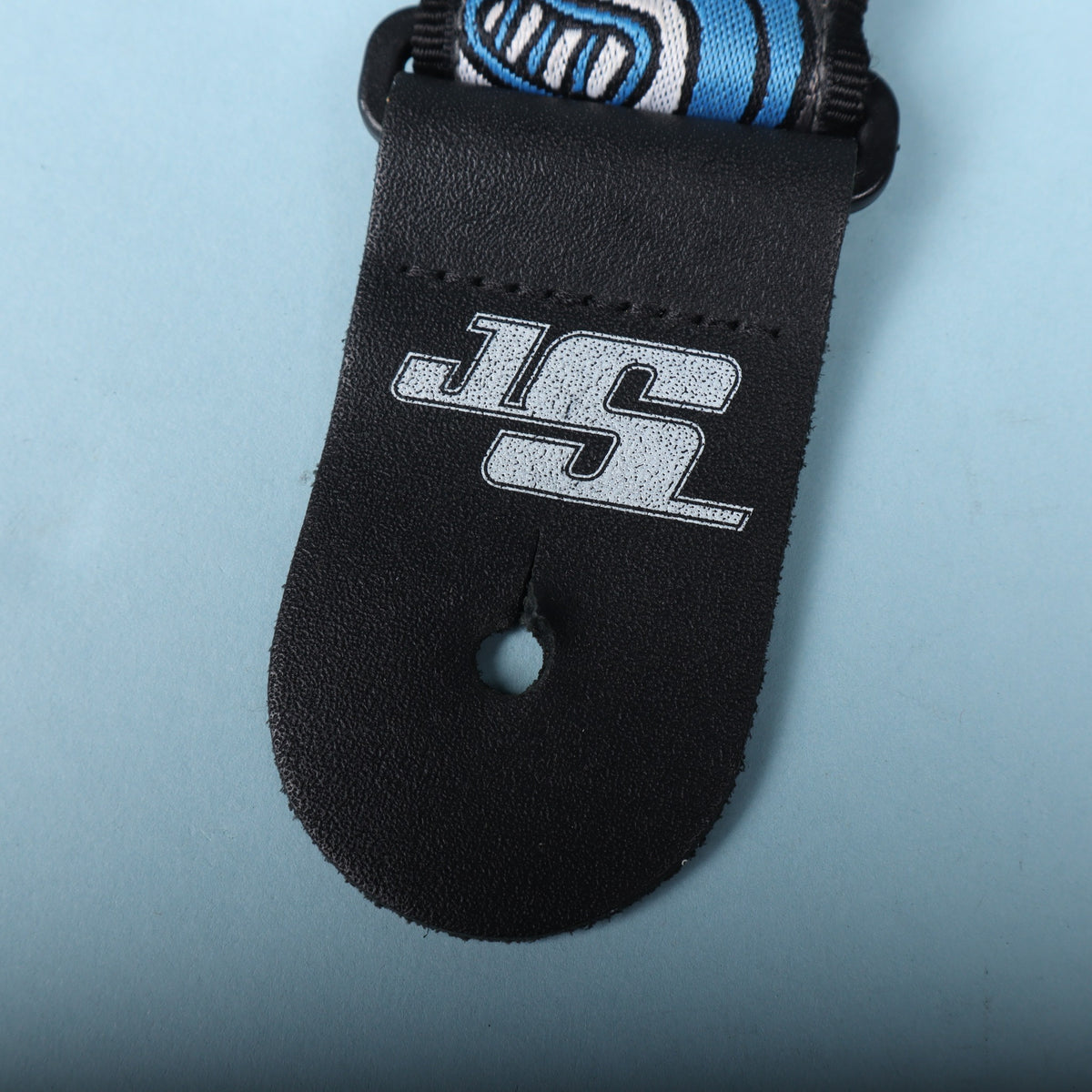 Close-up of the black leather strap end tab stamped with the silver JS logo