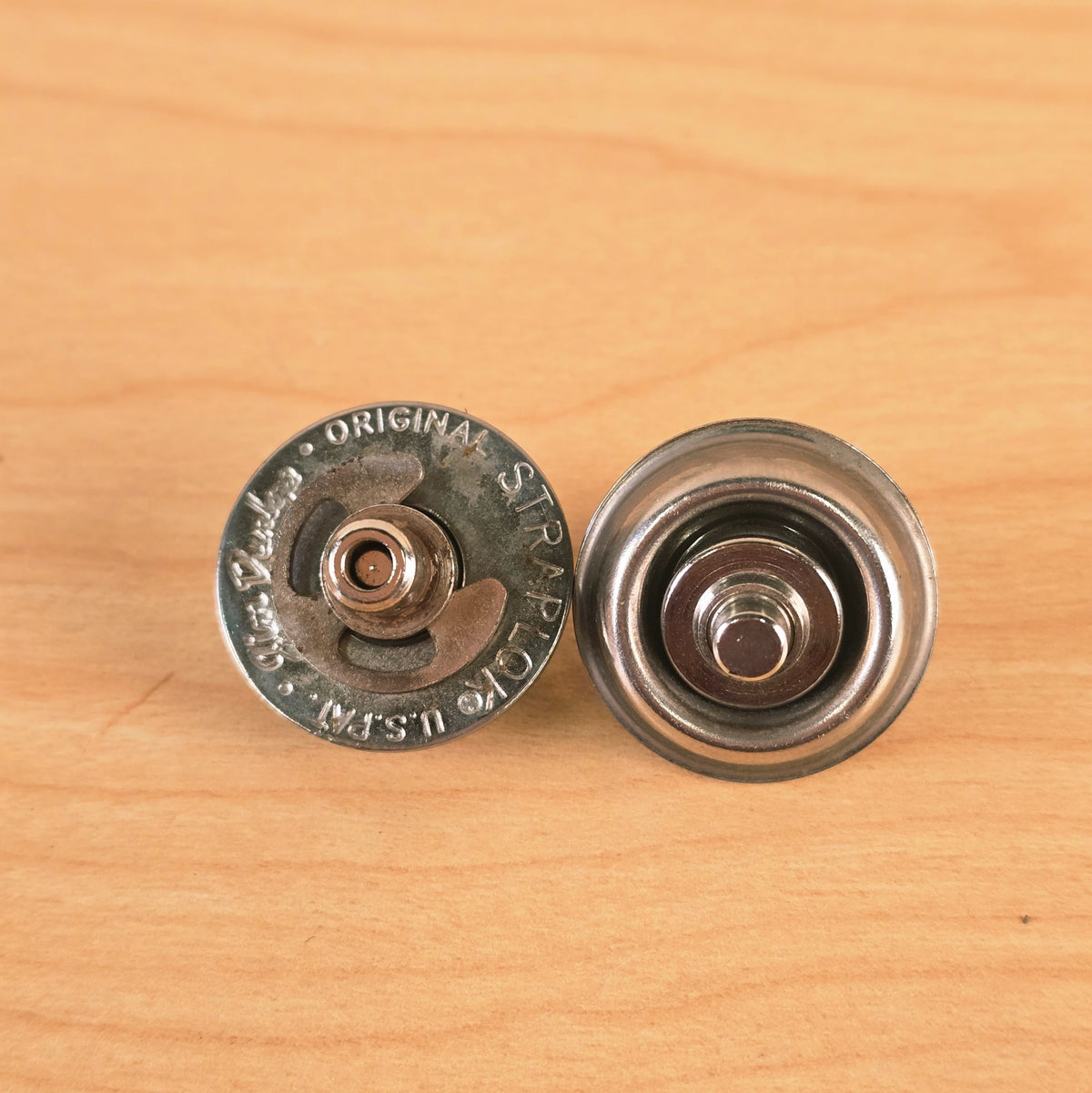Top-down view of two Jim Dunlop Original Straplok metal strap lock mechanisms on a wooden surface.