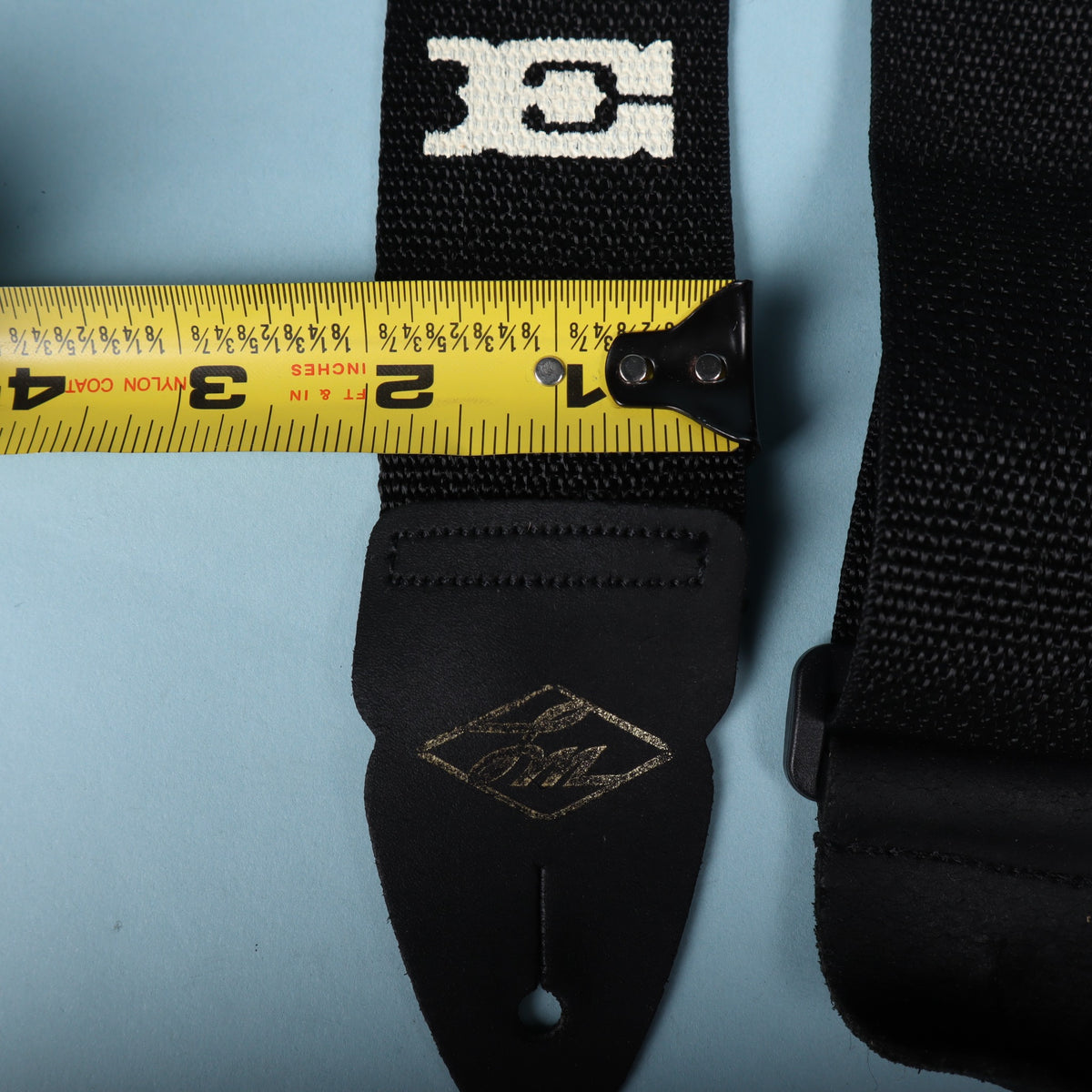 Close-up of the LM branded leather end tab alongside a tape measure showing a 2-inch width