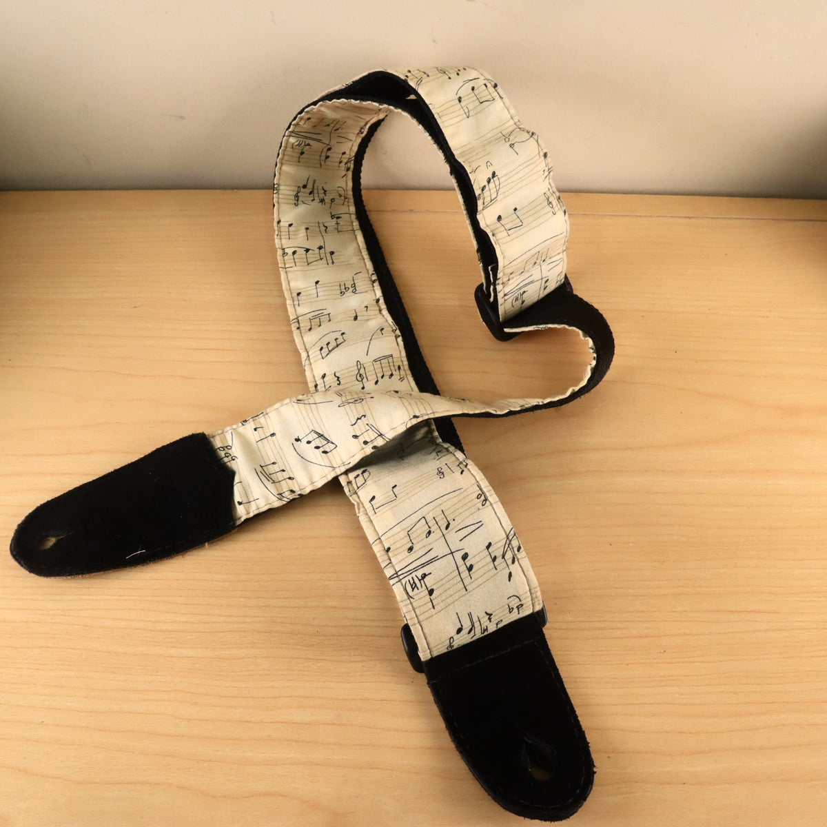 Full-length view of the sheet music fabric guitar strap arranged on a wooden surface.
