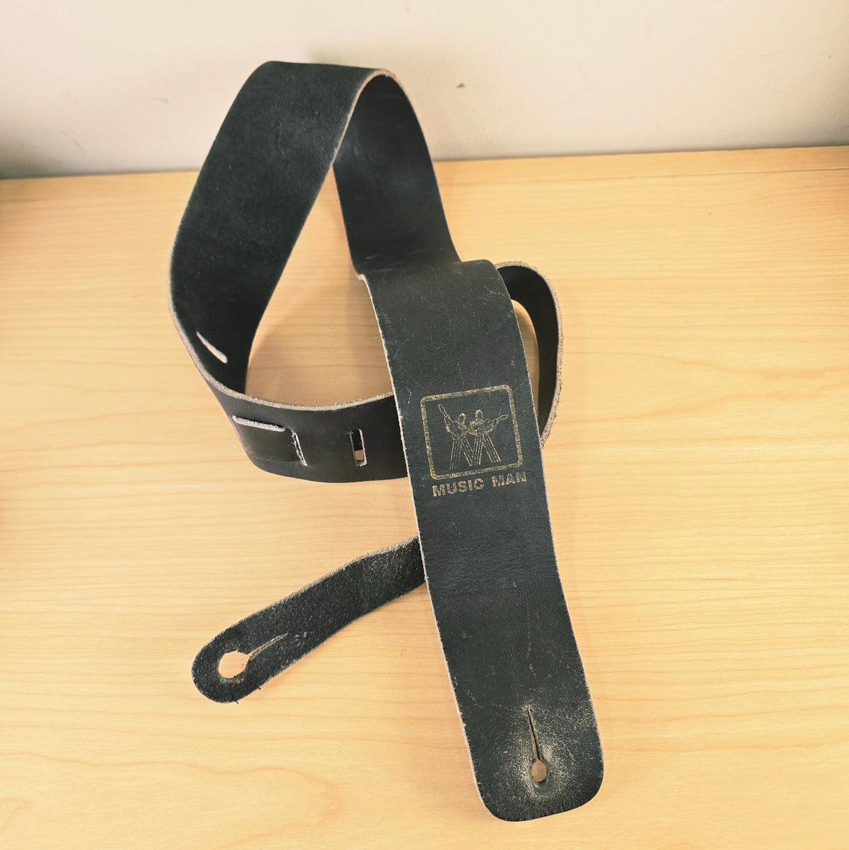 Front view of looped vintage Music Man black leather strap displaying adjustment tail