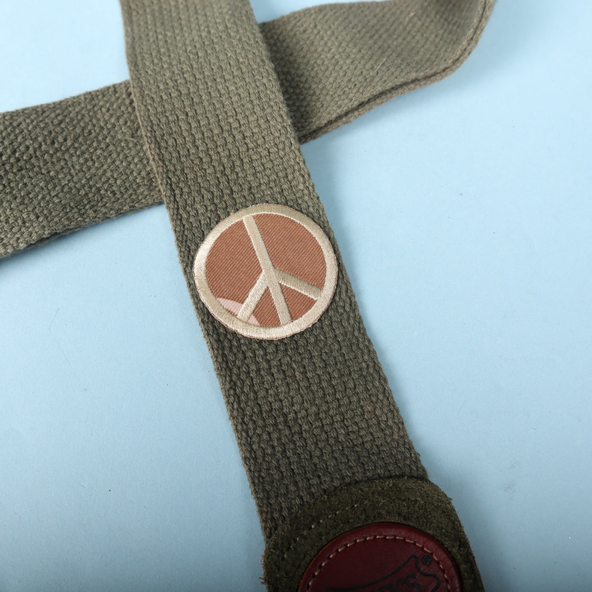Close-up of the embroidered peace sign patch on olive green woven strap