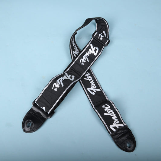 Overhead view of the black Fender running logo strap arranged in an X pattern on a blue background