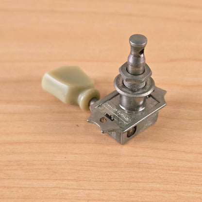 Angled view of string post, mounting plate, and keystone button on a wooden background.