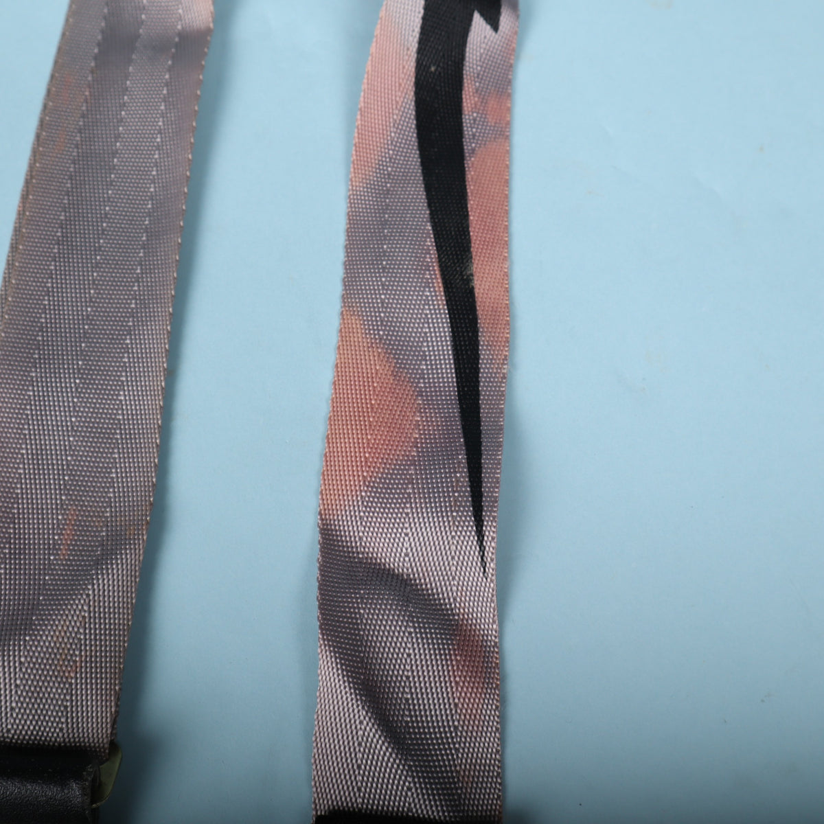 Detail of reddish discoloration and staining on the grey woven webbing alongside the black lightning bolt.
