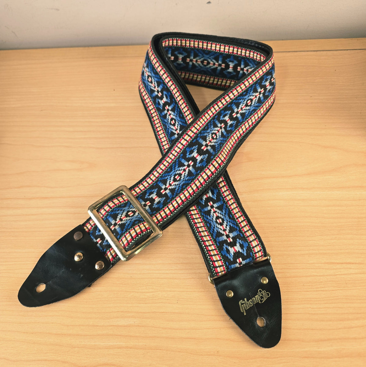 Full view of the vintage Gibson woven guitar strap laid out on a light wooden surface