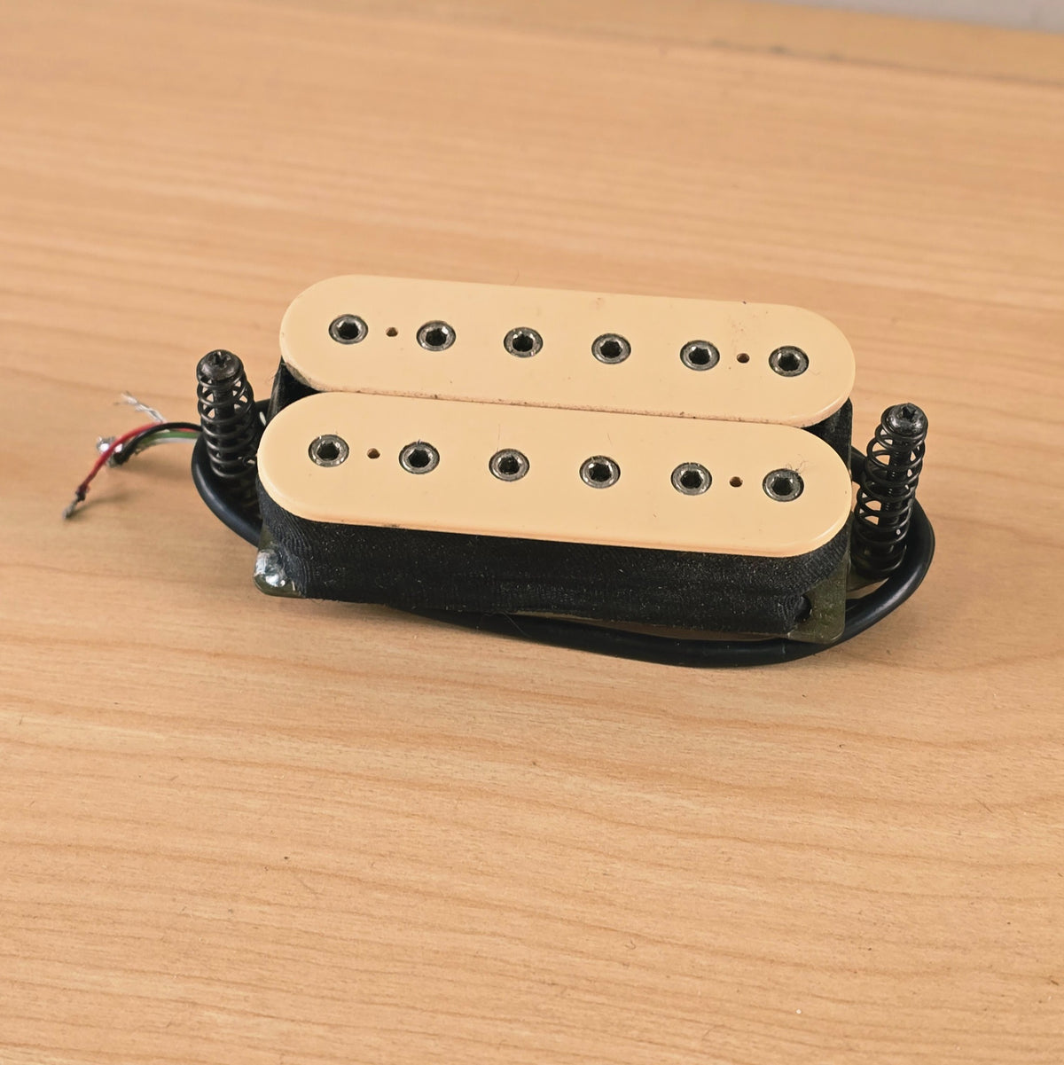 Three-quarter angle view of cream DiMarzio humbucker with mounting screws and springs