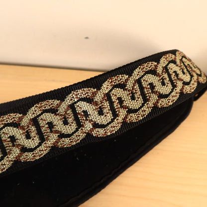 Close-up of the woven gold and brown Celtic pattern on the Planet Waves guitar strap.