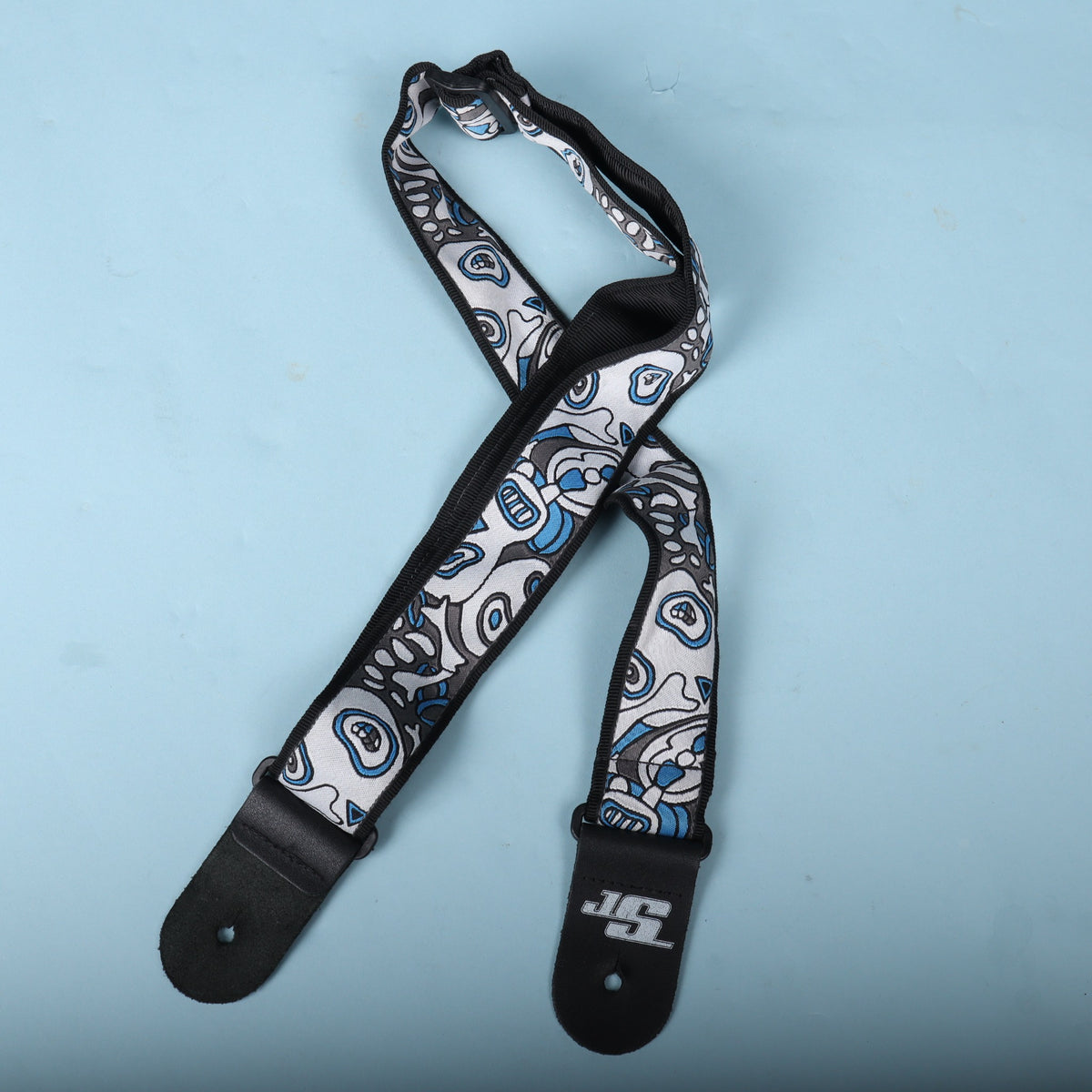 Planet Waves Joe Satriani guitar strap loosely coiled on a blue surface