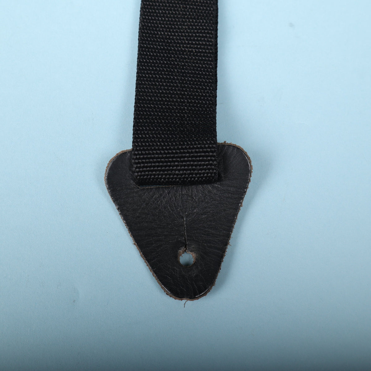 Close-up of the black leather end tab with keyhole slot attached to nylon webbing.