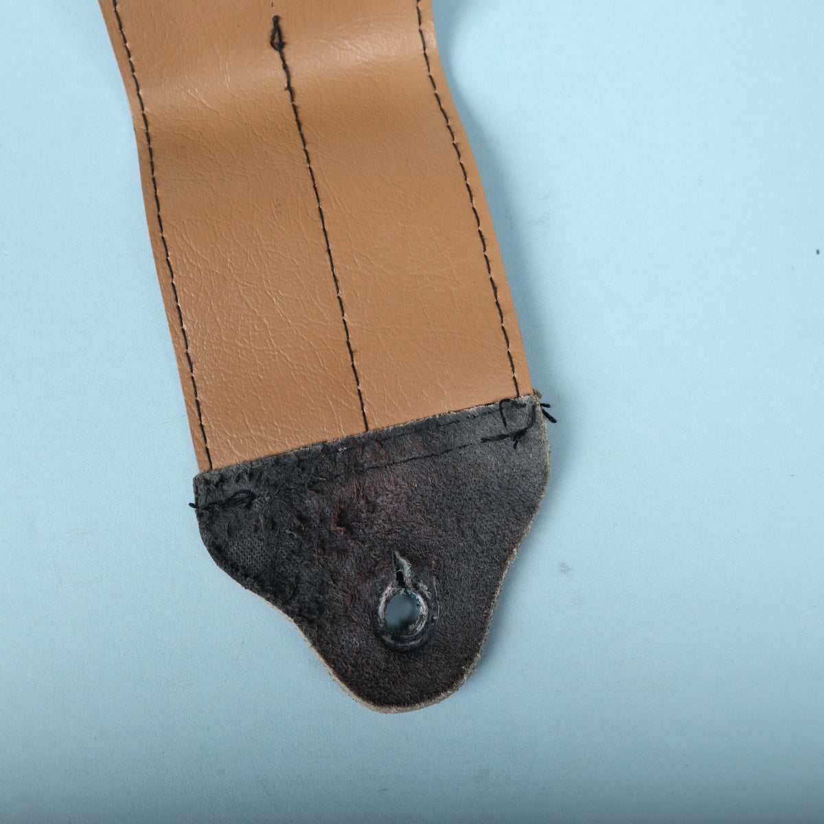 Close-up of the worn leather strap button tab and stitching on the tan vinyl backing.