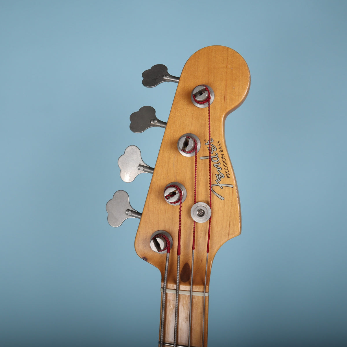 Front face of the headstock displaying the Fender Precision Bass spaghetti logo and string retainer.