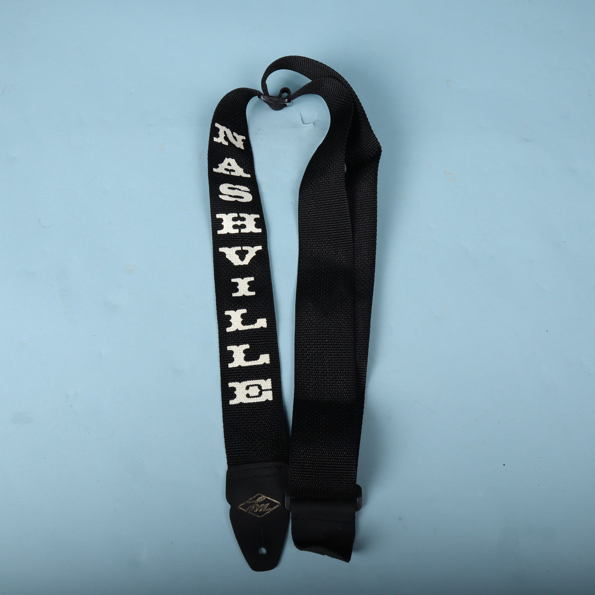Full view of the black LM Products Nashville guitar strap on a light blue background