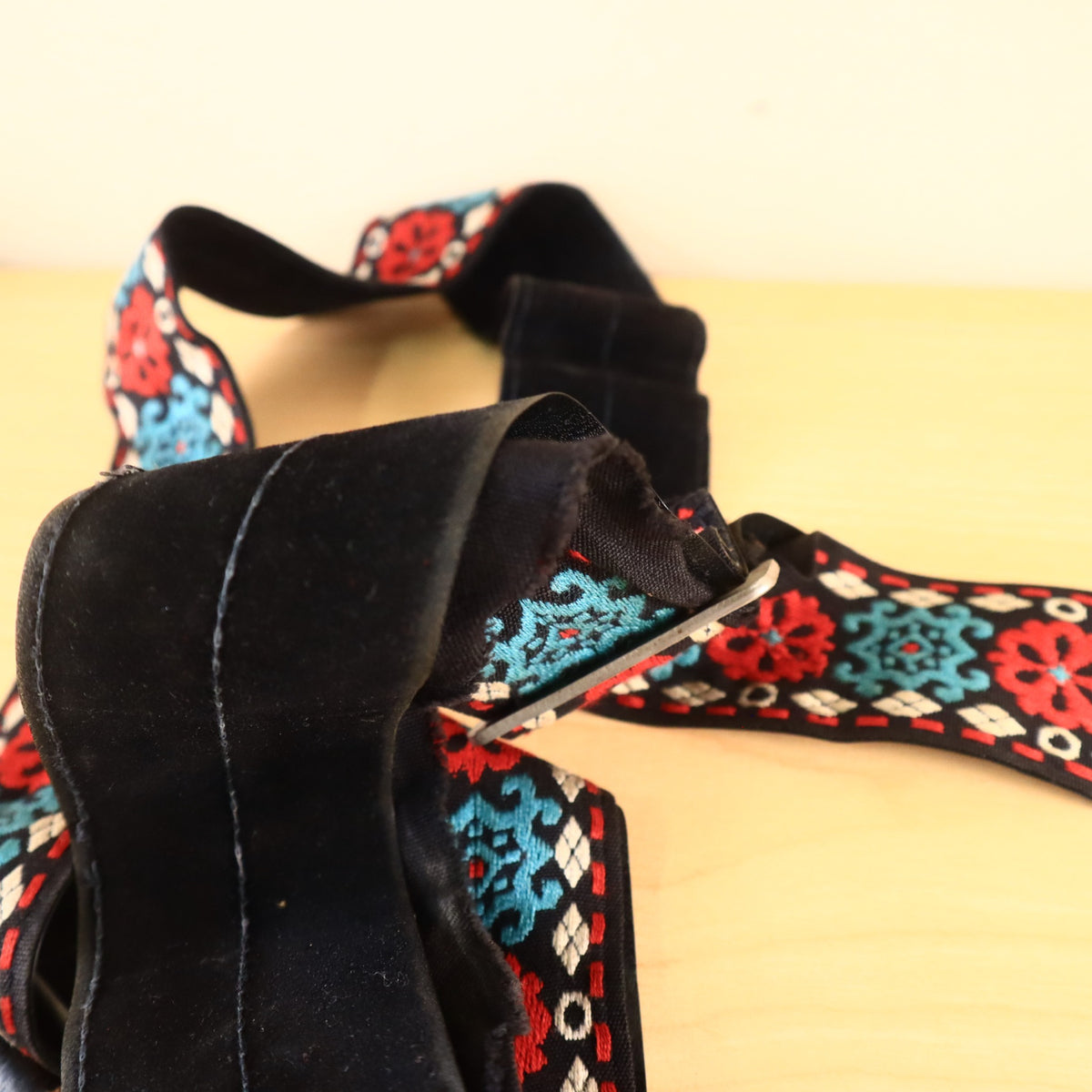 Folded guitar strap revealing black backing and red, teal, white pattern.