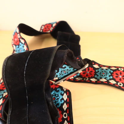Folded guitar strap revealing black backing and red, teal, white pattern.