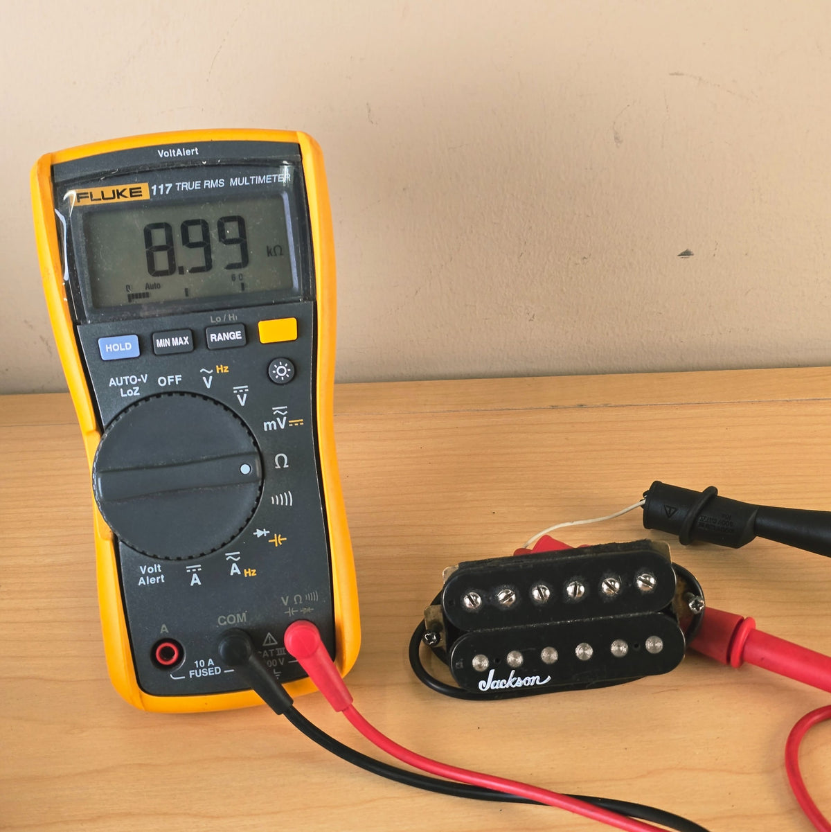 Digital multimeter displaying 8.99 kohms connected to a black Jackson humbucker pickup