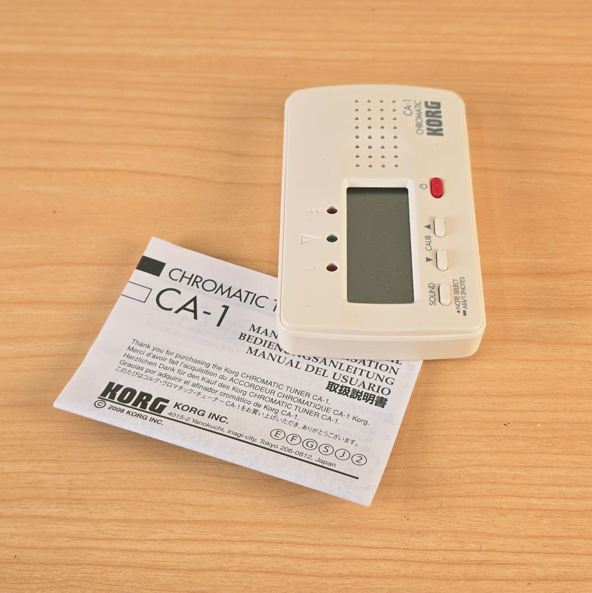 Upright vertical view of the Korg CA-1 digital chromatic tuner and manual.