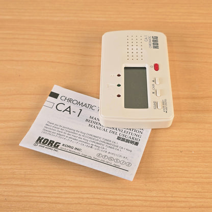 Upright vertical view of the Korg CA-1 digital chromatic tuner and manual.