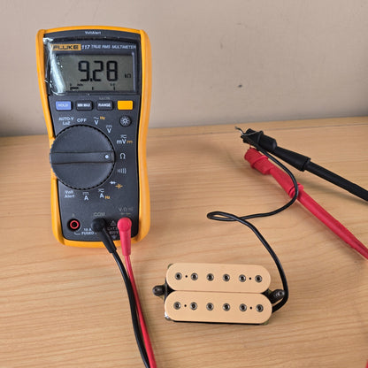 Fluke digital multimeter measuring 9.28 k-ohms DC resistance on a cream DiMarzio humbucker pickup