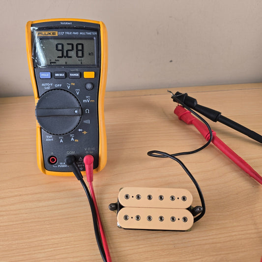 Fluke digital multimeter measuring 9.28 k-ohms DC resistance on a cream DiMarzio humbucker pickup