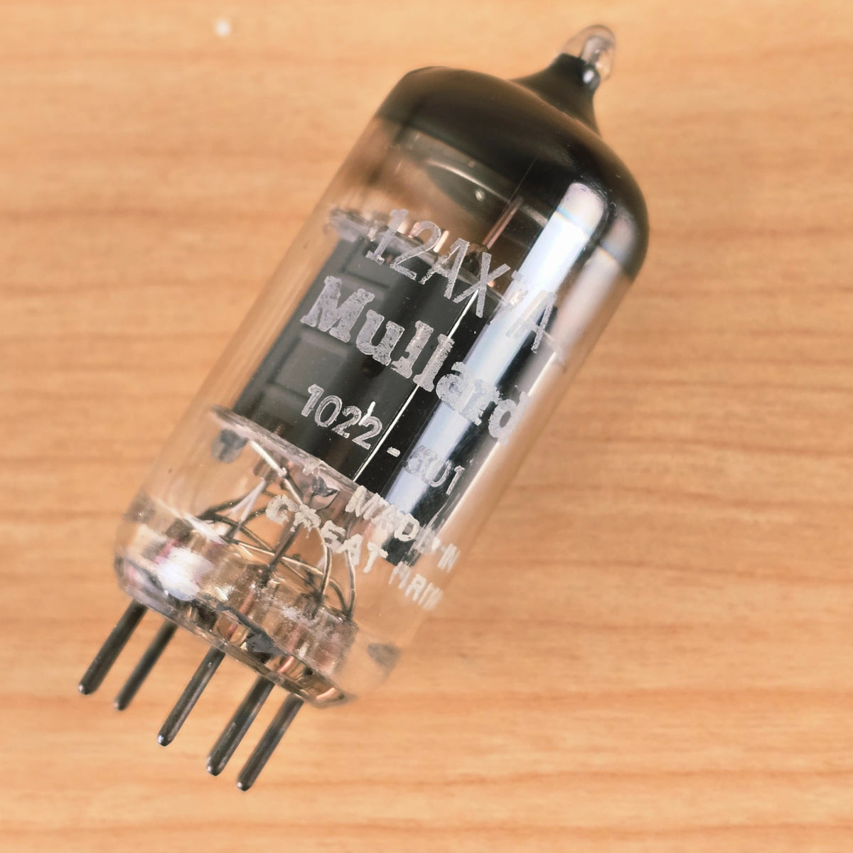 Angled view of Mullard 12AX7A vacuum tube lying on wood surface.