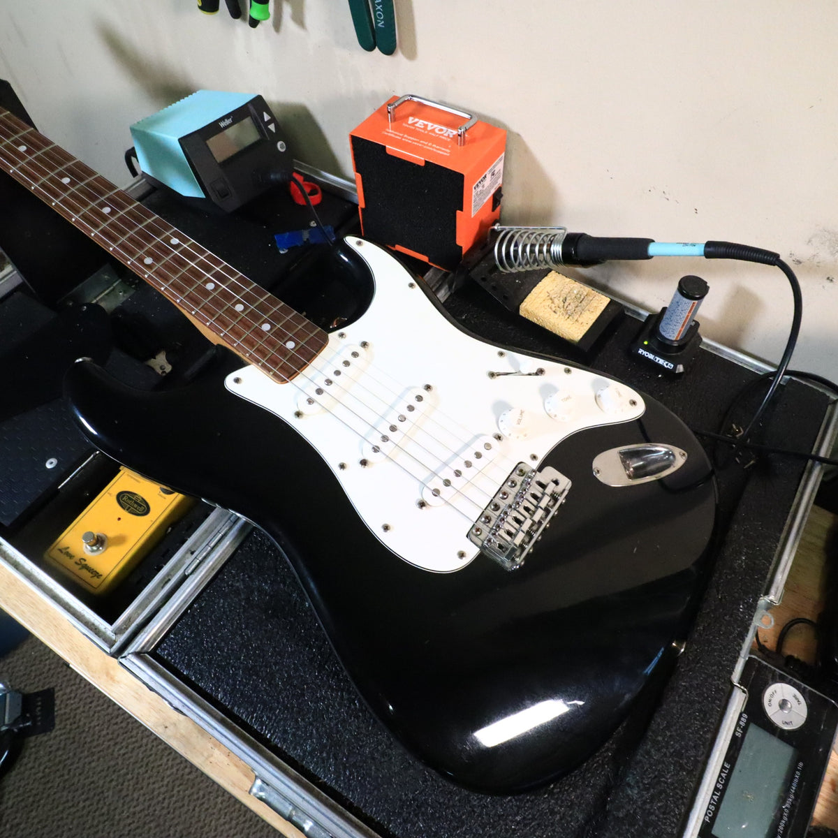 Squier Stratocaster electric guitar in black finish on work bench with tools.
