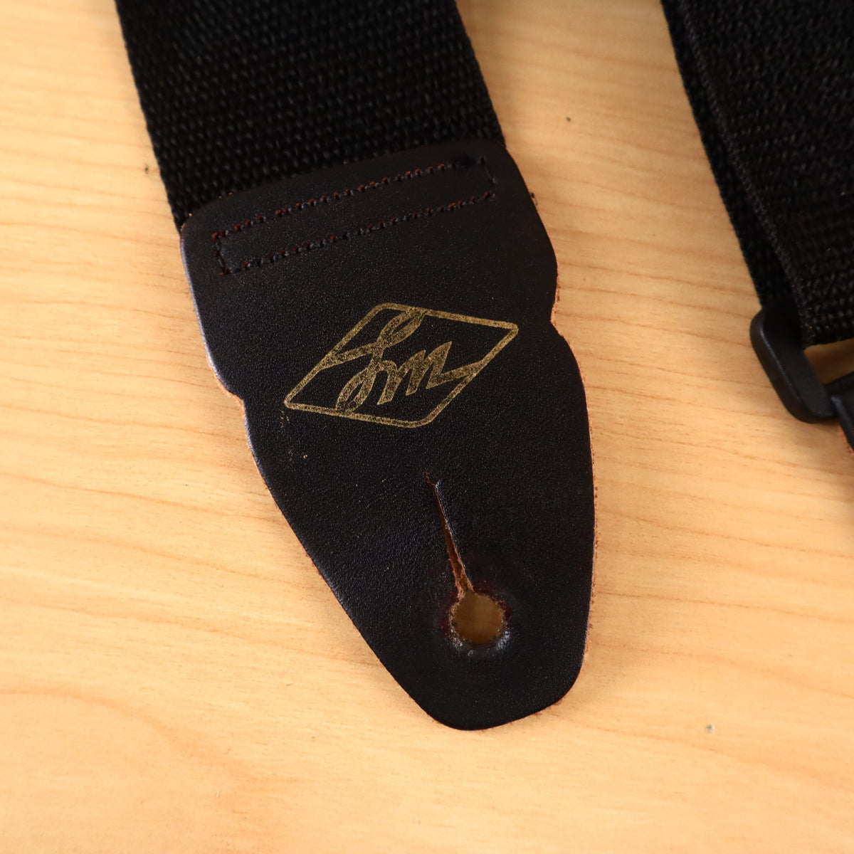 Close-up of black leather strap end showing gold embossed diamond LM logo.