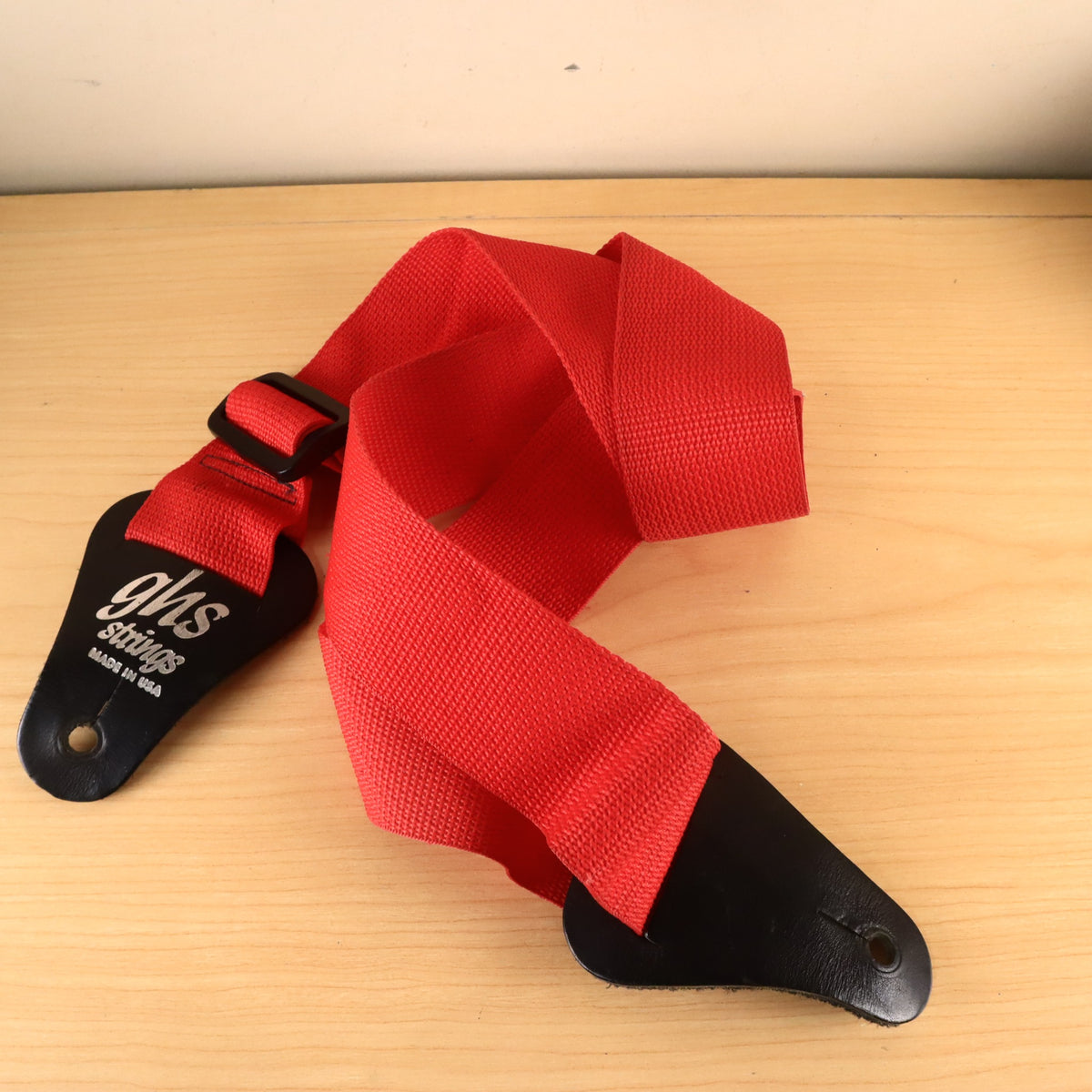 Full view of red GHS guitar strap arranged on a wooden surface.
