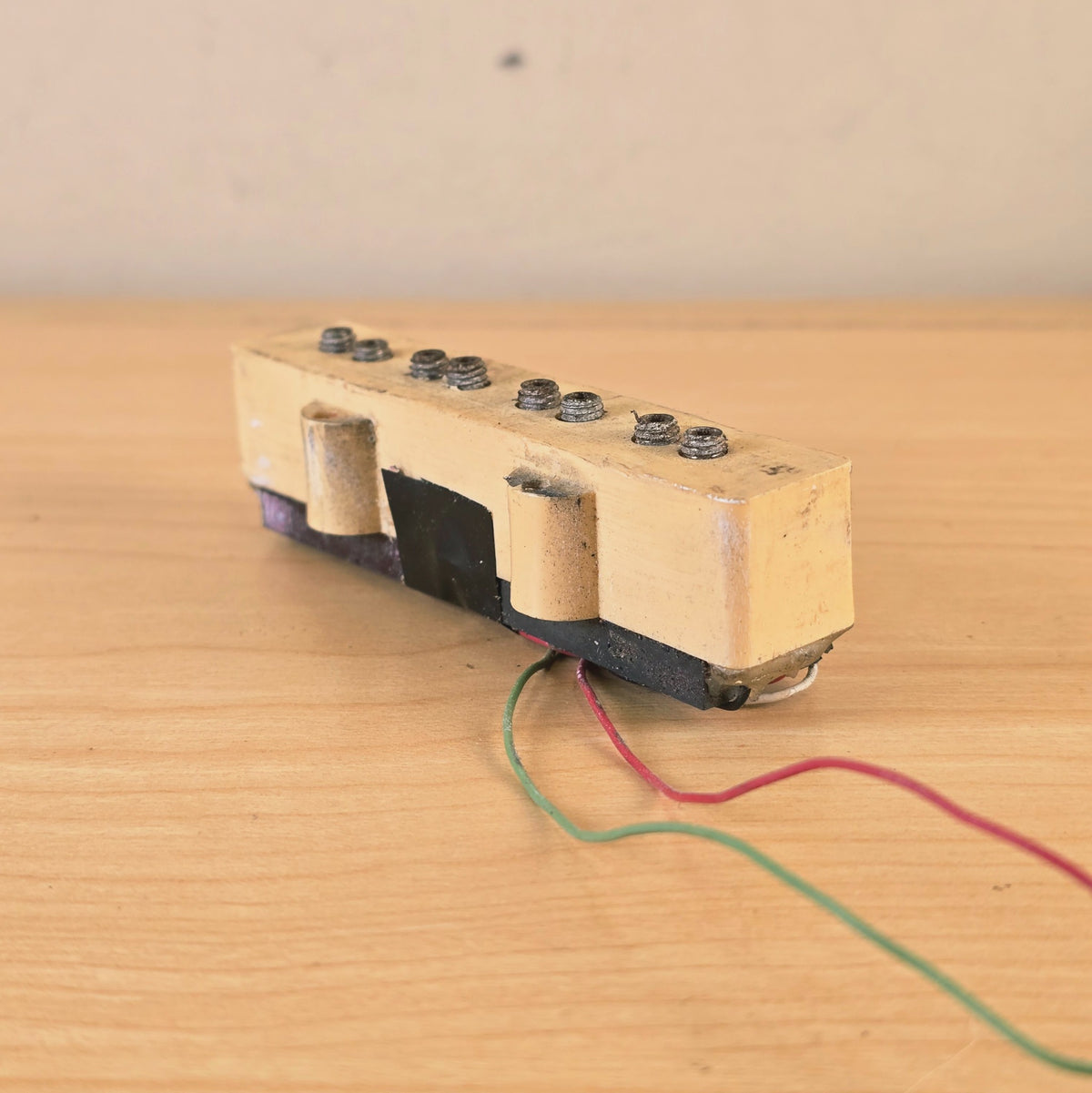 Angled side view of cream bass pickup on a wooden surface.