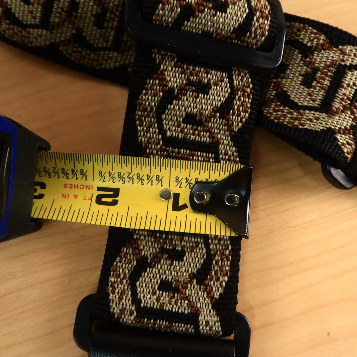 A yellow tape measure showing the 2-inch width of the Planet Waves woven guitar strap.