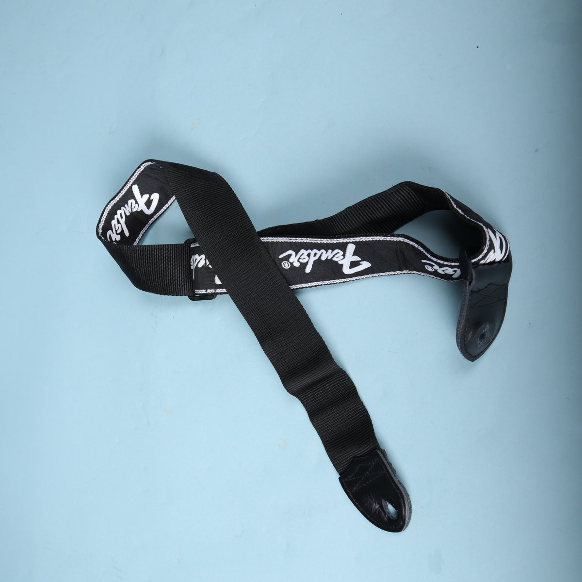 Full view of the coiled black Fender running logo guitar strap showing the underside and leather ends