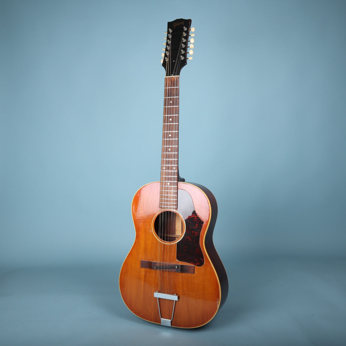 Full front view of a 1967 Gibson B-25-12 acoustic guitar on a blue background.