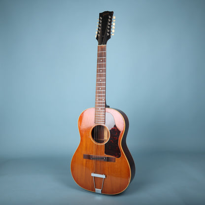 Full front view of a 1967 Gibson B-25-12 acoustic guitar on a blue background.