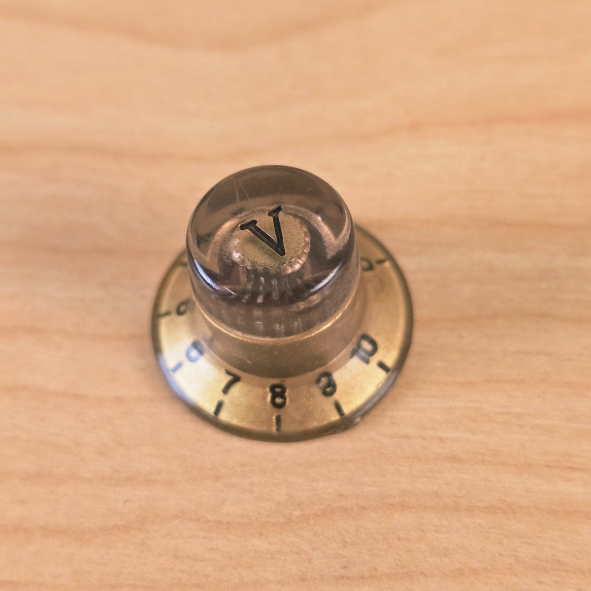Top view of gold and transparent top hat knob with V marker on wooden surface