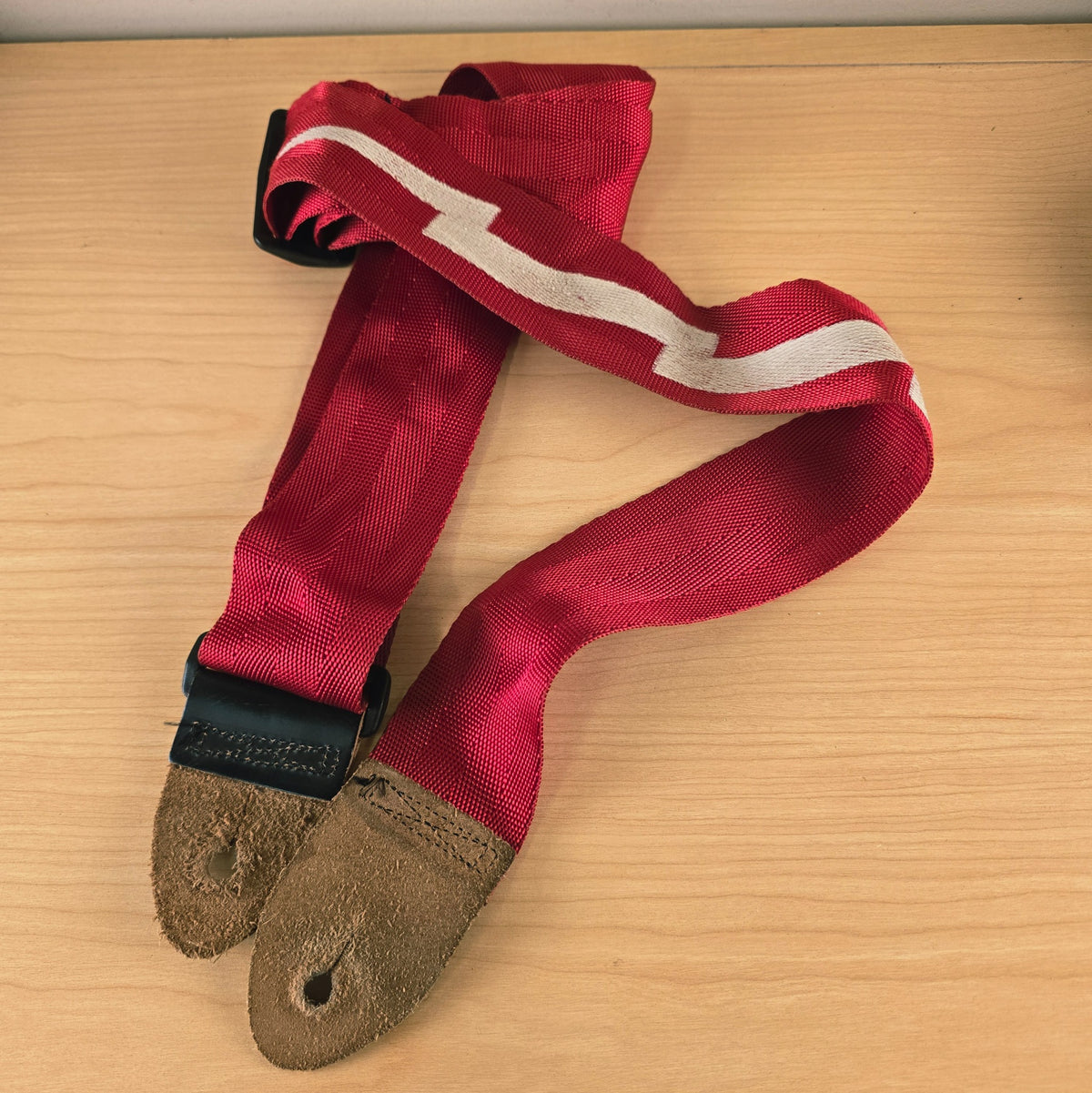 Full view of the red Gibson lightning bolt guitar strap folded on a wooden table