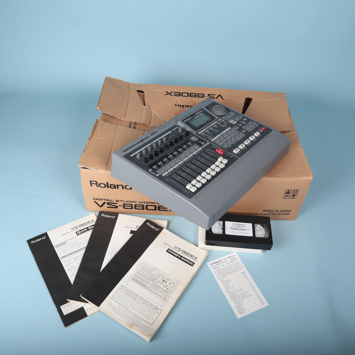 High-angle view of Roland VS-880EX digital multitrack recorder with manuals, cassette tape, and box.