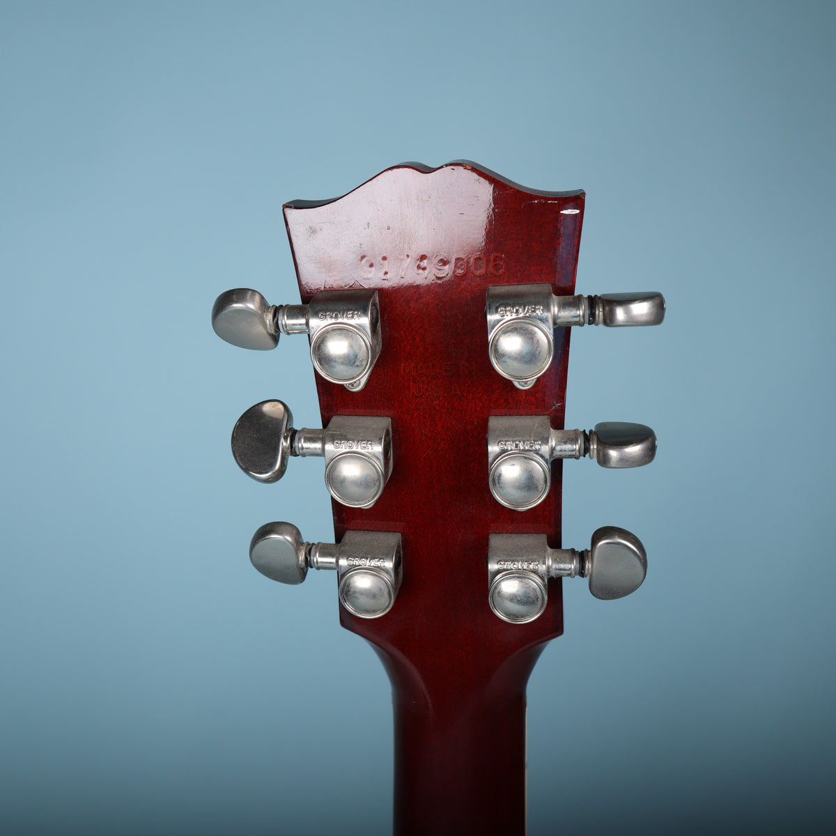 Headstock rear showcasing Grover tuners and the stamped serial number on blue background.