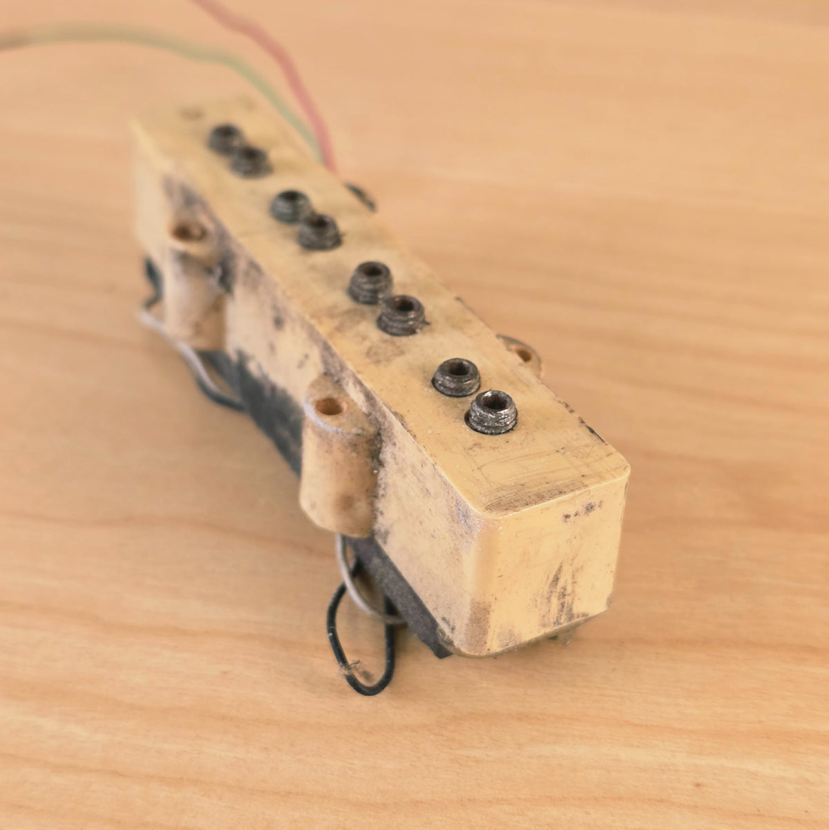 Angled perspective view of cream bass pickup cover and pole pieces.