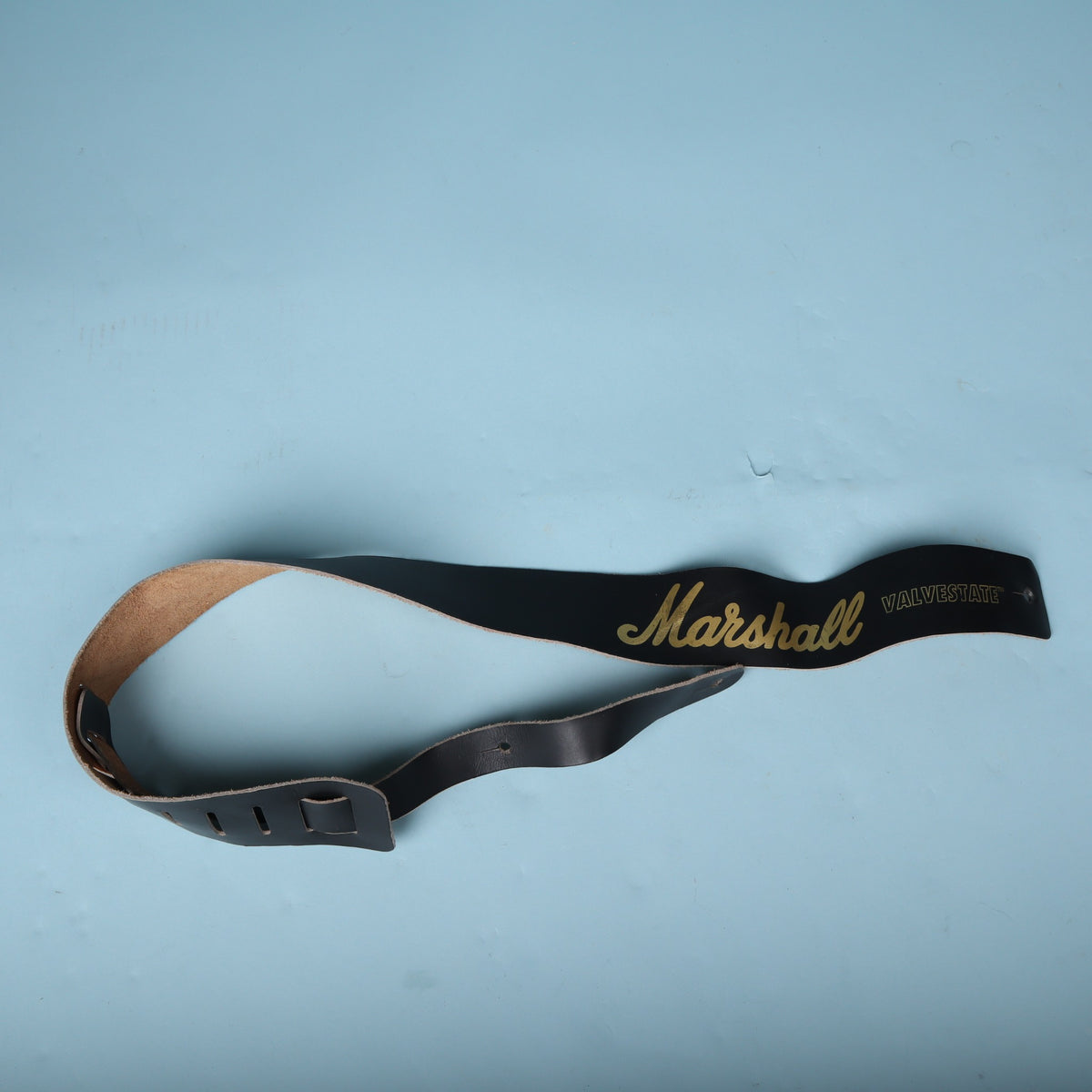 Full view of the black Marshall Valvestate leather guitar strap on a light blue background