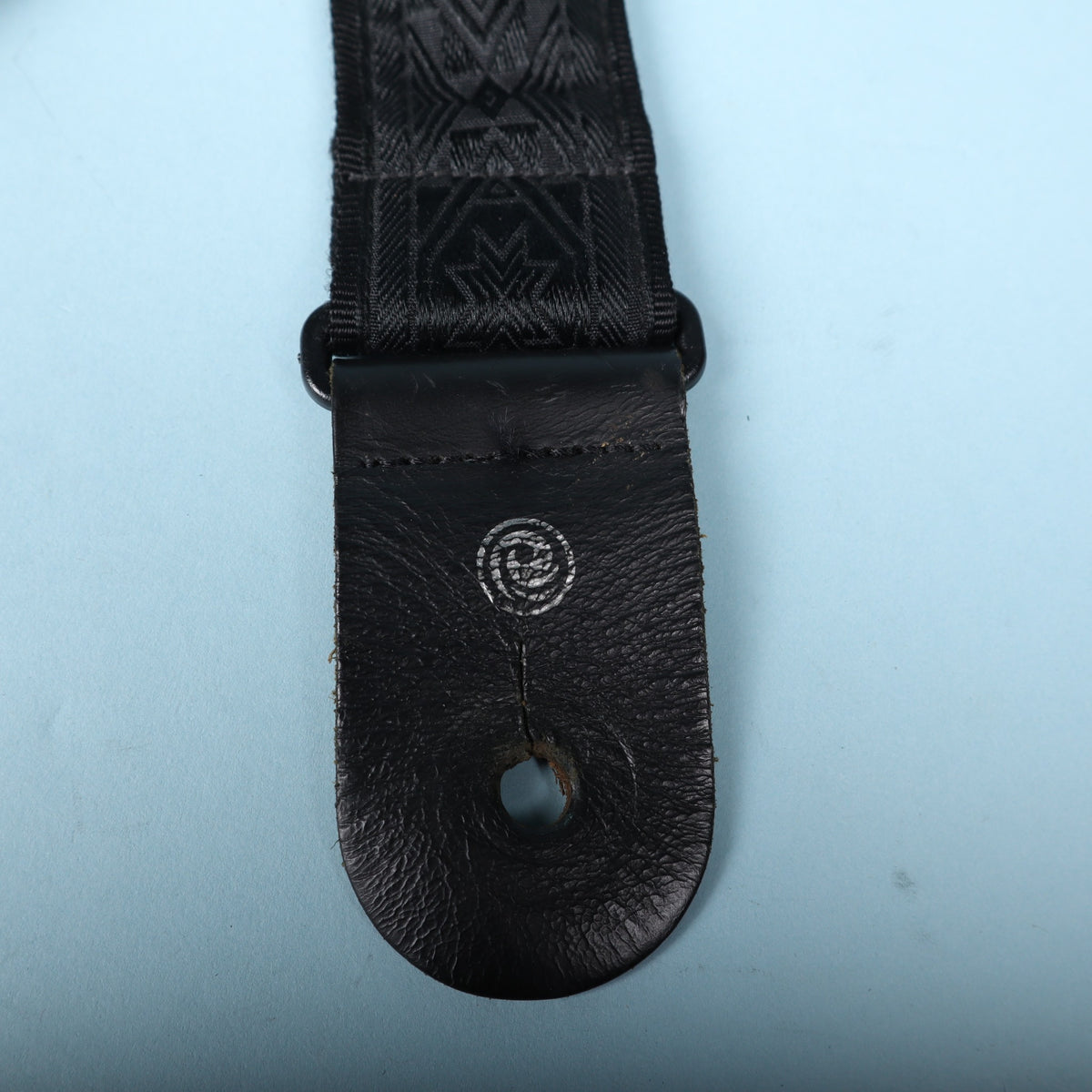 Detailed view of the black leather end tab with silver Planet Waves logo stamp.
