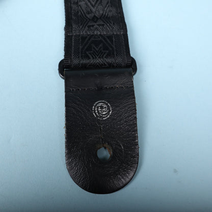 Detailed view of the black leather end tab with silver Planet Waves logo stamp.
