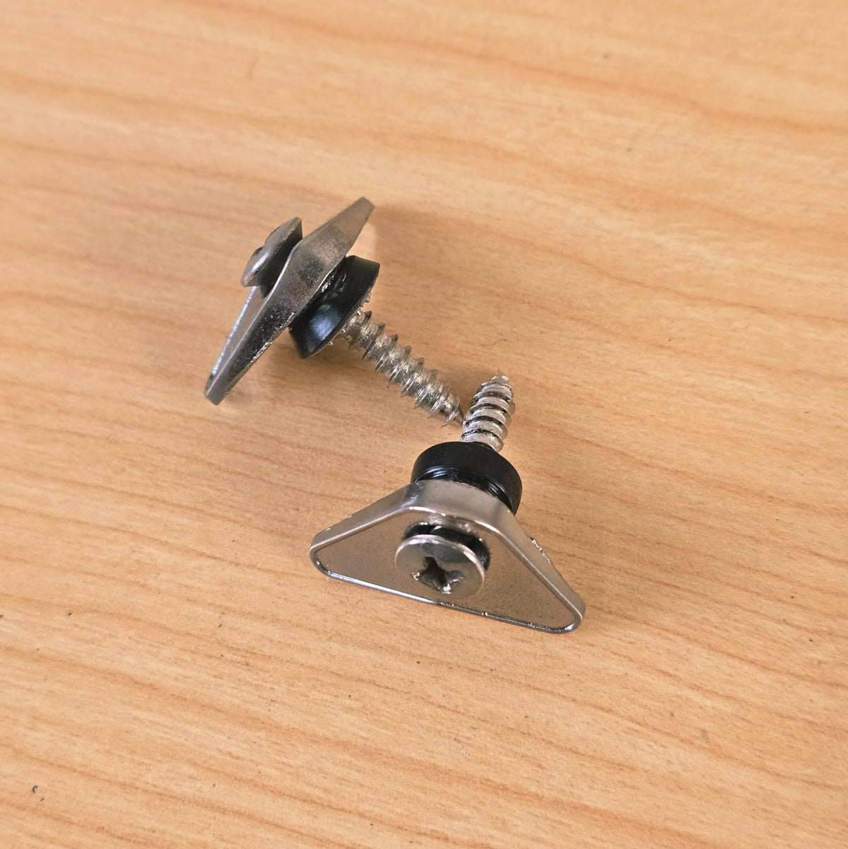 Side view of two chrome triangular guitar string retainers with attached hardware.