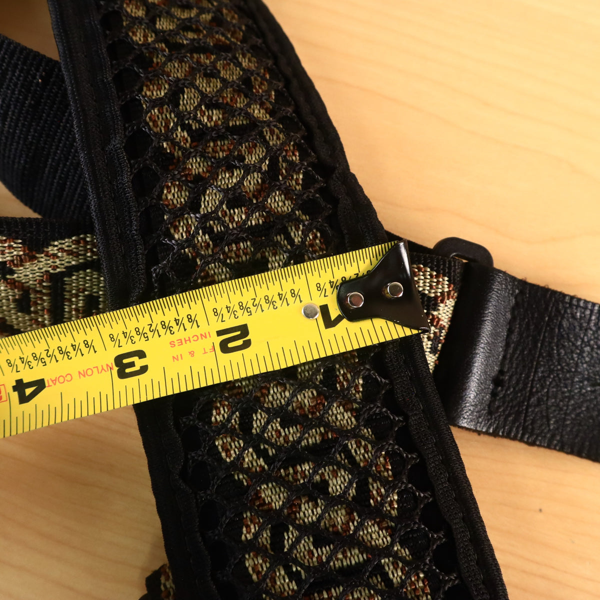 A yellow tape measure showing the 3-inch width of the padded mesh bass shoulder pad.