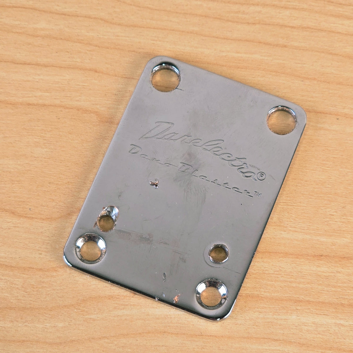 Angled view displaying the chrome surface and mounting holes of the Danelectro neck plate.