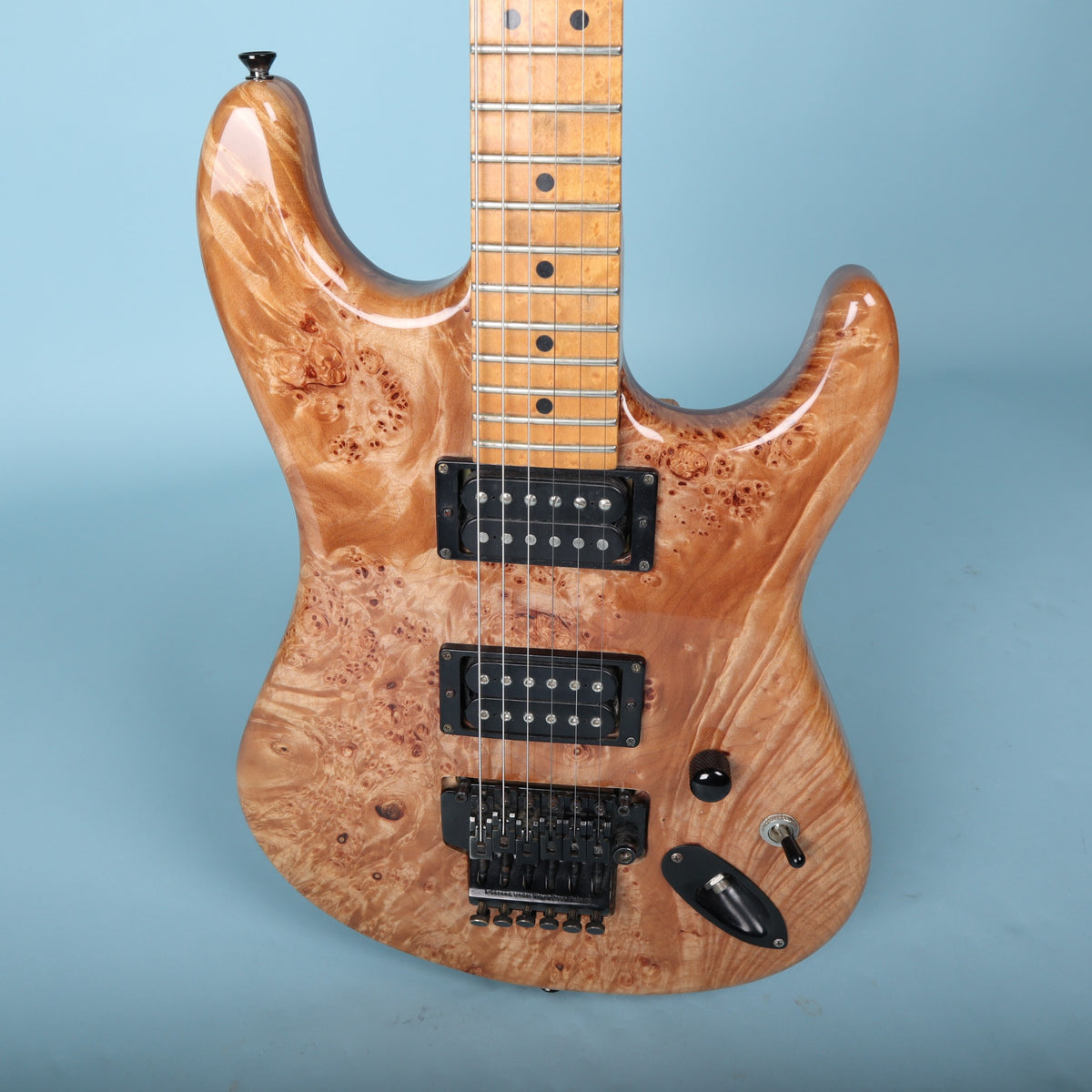 Close-up of burl top guitar body with black hardware and control switches.