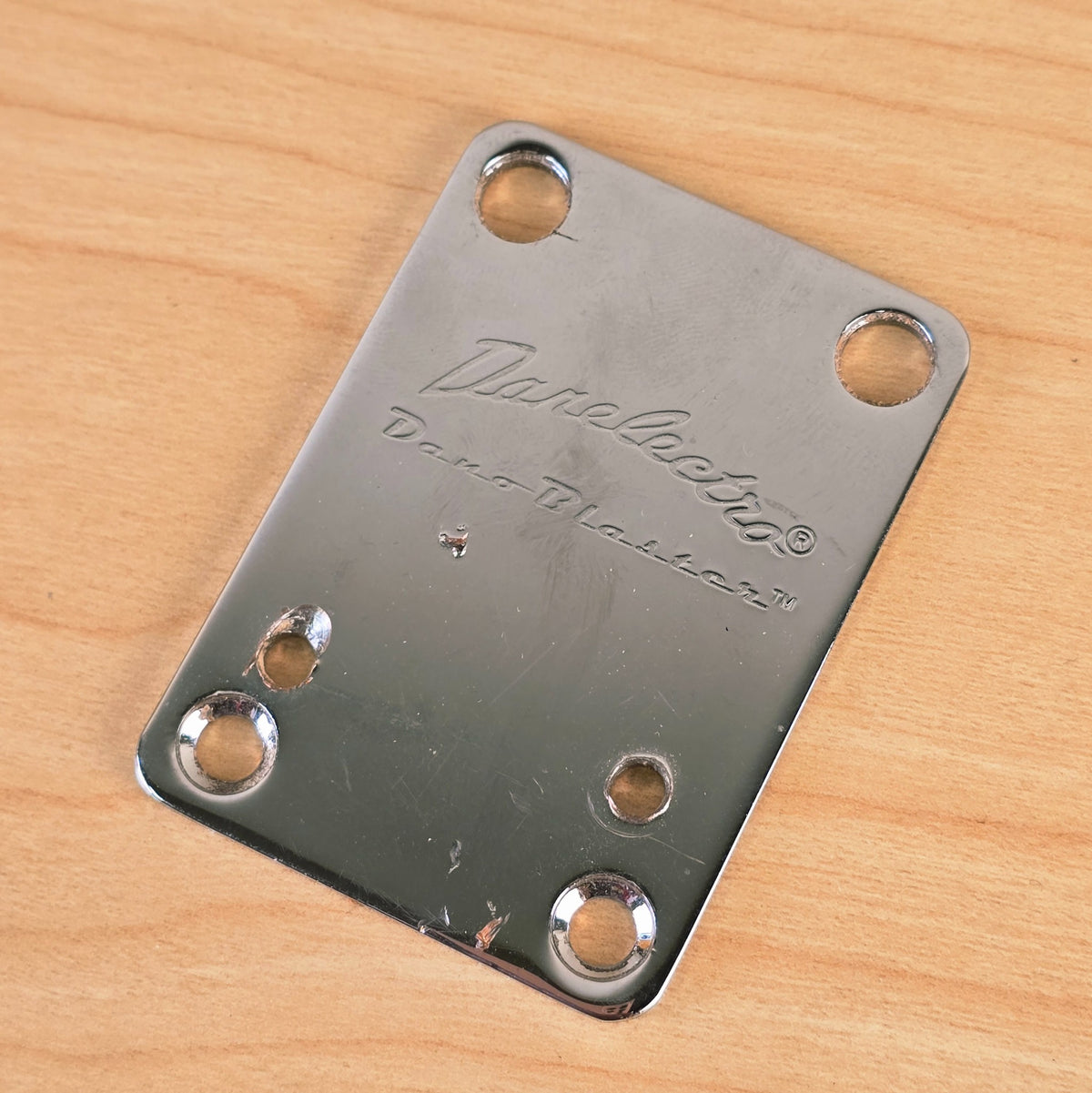 Front view of a chrome Danelectro Dano-Blaster guitar neck plate with engraved logos.