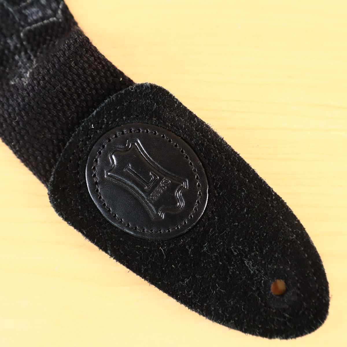 Detail of the black leather end tab with embossed Levy's logo badge and button hole.